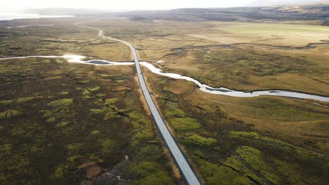 beautiful aerial of a distant car driving over a long road running through a stunning icelandic landscape on a sunny day