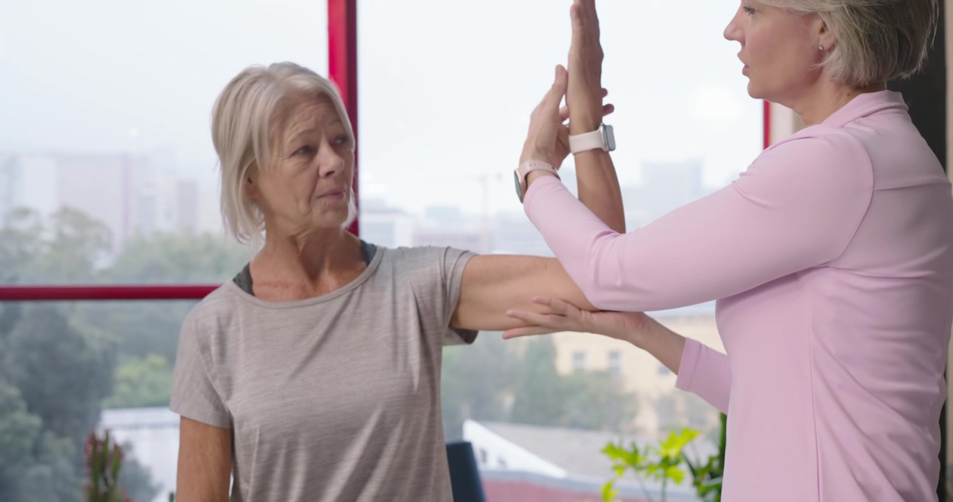 Female clinician greeting female patient, guiding, supporting arm on treatment table for assessment