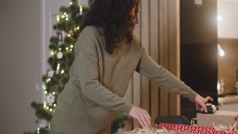 mujer morena envolviendo regalos de navidad en una mesa en una habitación decorada con un árbol de navidad 2