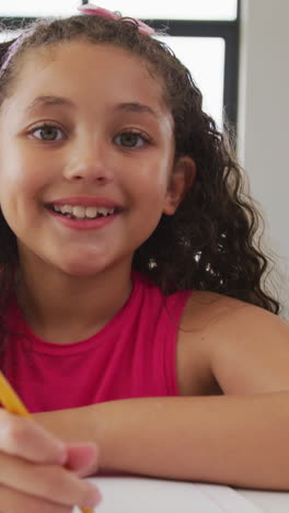 video of happy biracial girl sitting at school desk and learning