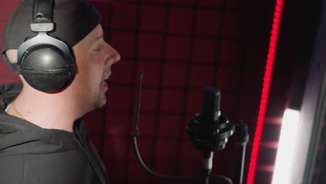 a man dressed in black, passionately singing into a microphone in a soundproofed recording room. the singer is wearing headphones and making expressive hand movements, fully immersed in the music