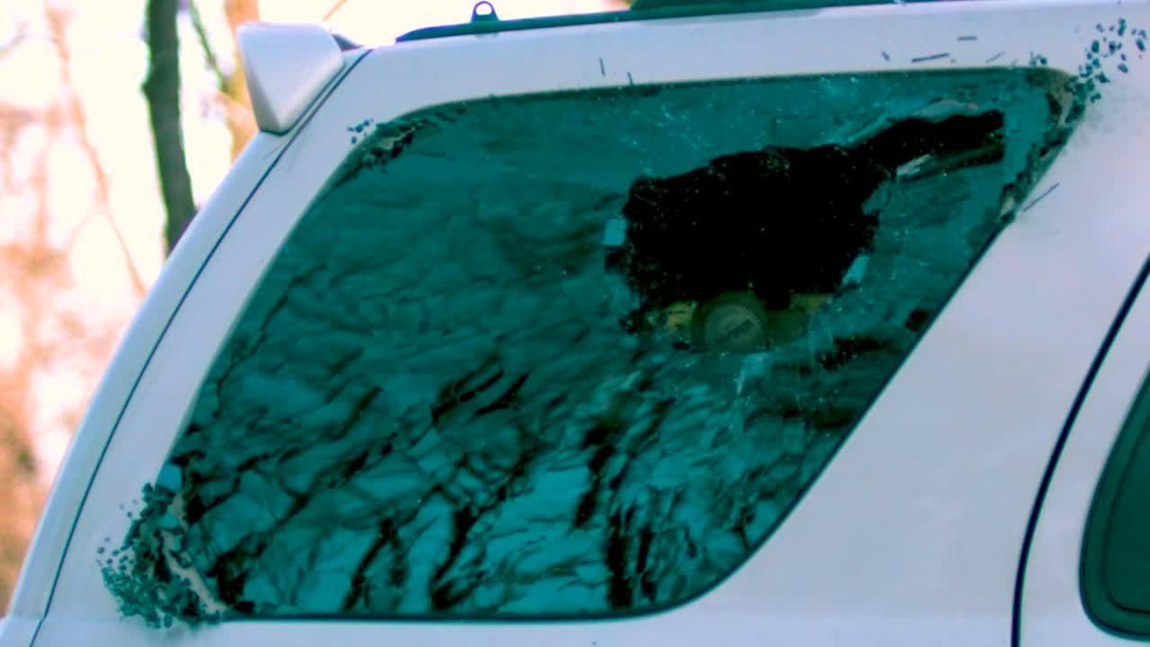 A baseball being thrown into a cars side window breaking it to pieces with glass shattering and flying around in slow motion