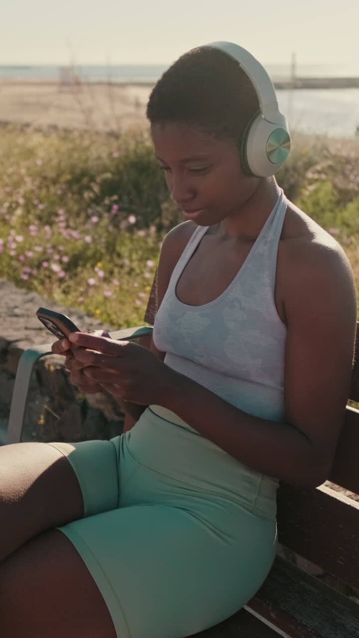Young Black Woman with Headphones Using Phone on Outdoor Bench