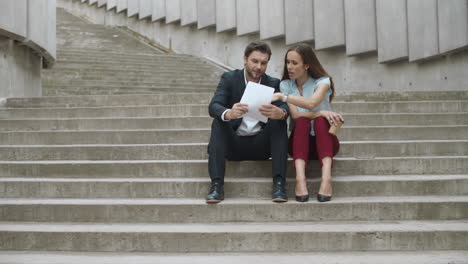 compañeros de trabajo sonrientes buscando buenos resultados de trabajo en documentos en la ciudad moderna