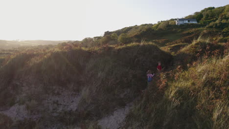 drone shot of young boy and girl on beach vacation playing in sand dunes with evening light