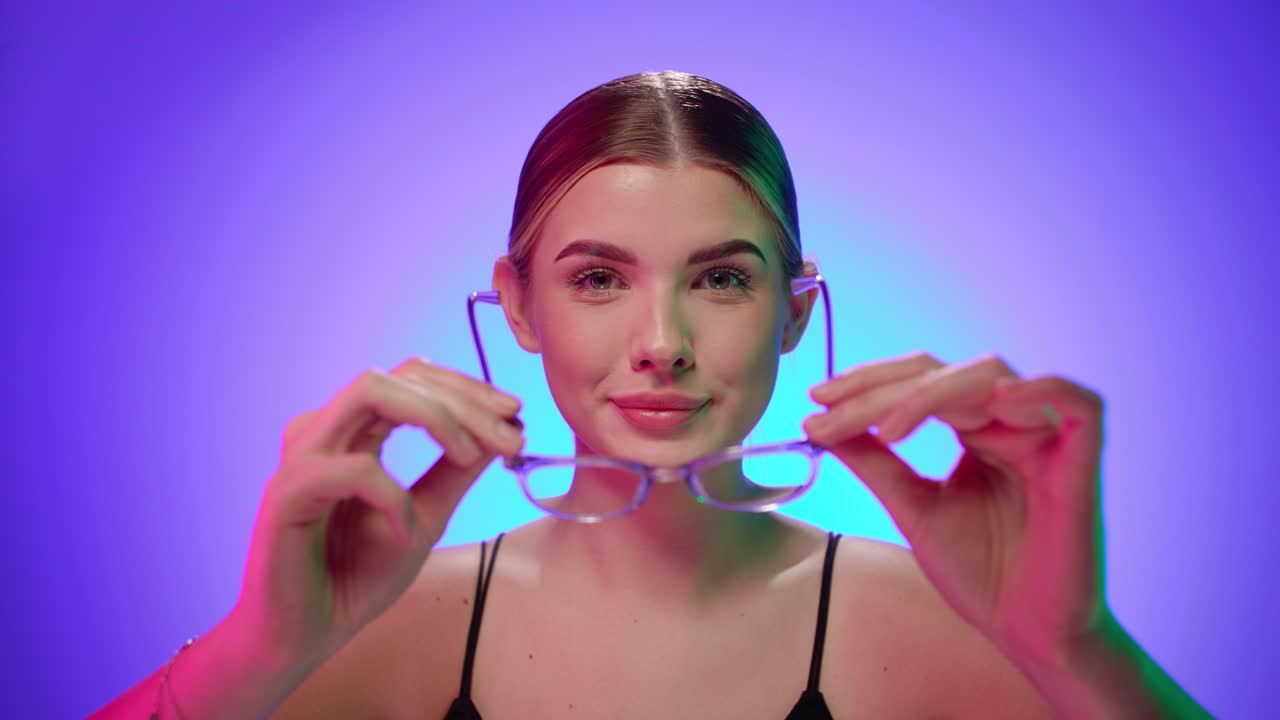 매력적인 금발 여성은 카메라 앞에서 독서 안경을 가지고 놀고, 맨 몸으로 스튜디오에서 찍은 가까운 초상화입니다.