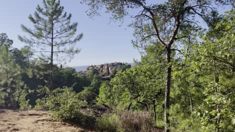 Shot-through-a-forest-in-France-on-a-small-hill-with-a-small-village-in-France-with-many-small-old-stone-houses-in-good-weather