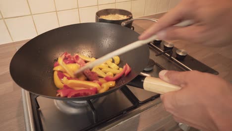 stir-frying of red and yellow sweet peppers in a wok