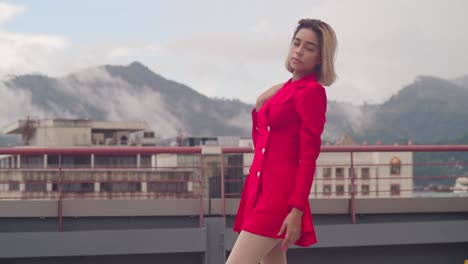 a short red dress adorns a young hispanic girl as she gazes out from the city rooftop