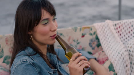 slow motion beautiful young asian woman drinking beer enjoying rooftop party sitting on couch sipping refreshing beer celebrating friendship