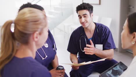 Video-of-biracial-male-doctor-talking-with-diverse-female-doctors-in-hospital-meeting