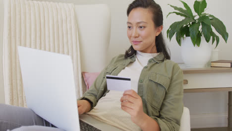 Happy-asian-woman-using-laptop-and-holding-credit-card-in-bedroom,-in-slow-motion