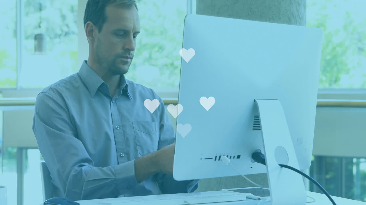 Male office worker interacting with health app on computer at desk, displaying floating heart icons
