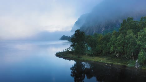 Una-Fina-Niebla-Matutina-Se-Cierne-Sobre-Las-Tranquilas-Aguas-Del-Lago-Y-Envuelve-Montañas-Cubiertas-De-Bosques.