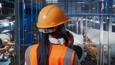 close up back view of asian female engineer with safety helmet talking on smartphone while standing in factory manufacture of wind turbines