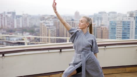 mujer elegante con una elegante túnica azul practicando yoga en la terraza