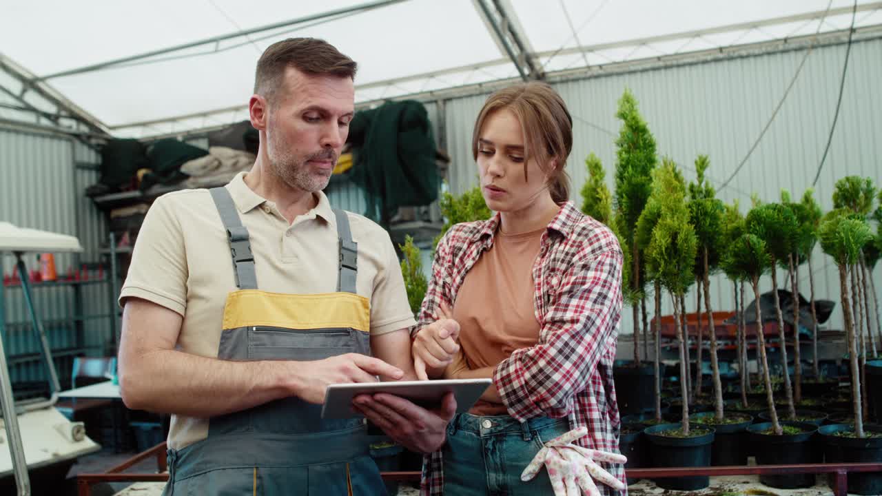 Due botanici caucasici concentrati che lavorano in serra e usano un tablet.