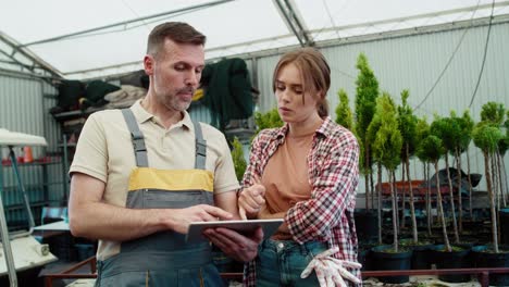 two focused caucasian botanists working in greenhouse and using tablet.