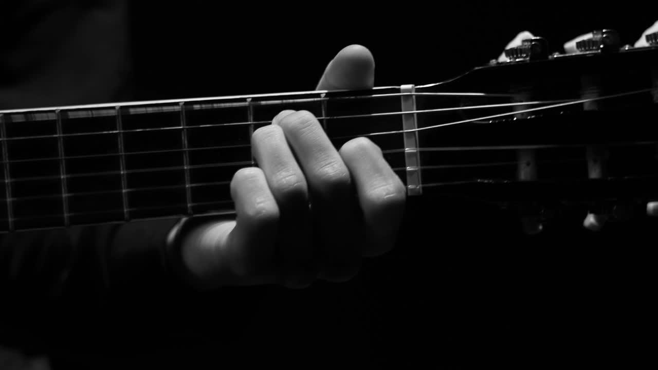 Black and white video of the left hand of a guy playing guitar