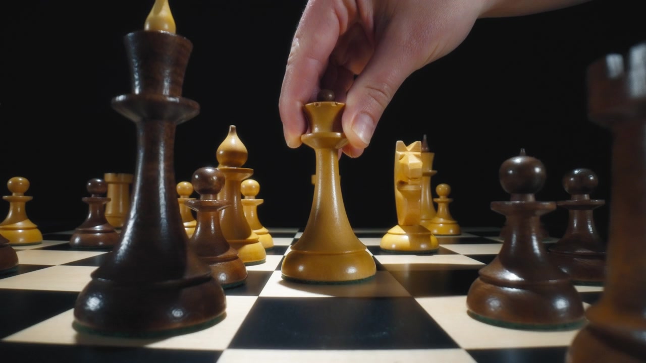 Player hand moving white queen chess piece on a chessboard