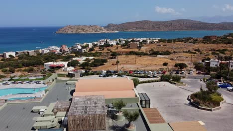 View-of-the-sea-at-CayoResort-in-Greece-Crete---Brunette-woman-in-swimming-costume-sits-at-the-pool-edge-and-drinks-cocktail---Drone-flies-fast-forwards-towards-the-sea