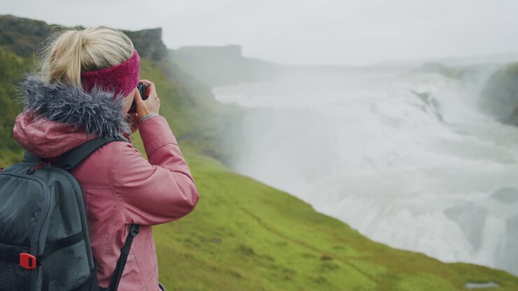 Tourist woman in rain photographing impressive Gullfoss waterfall. Famous attraction and landmark destination on Iceland on the Golden Circle