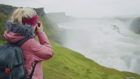 una turista en la lluvia fotografiando la impresionante cascada de gullfoss, una famosa atracción y destino histórico en islandia en el círculo dorado