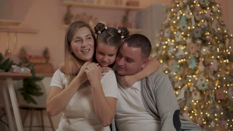 madre, padre y niña se besan y abrazan celebrando la navidad