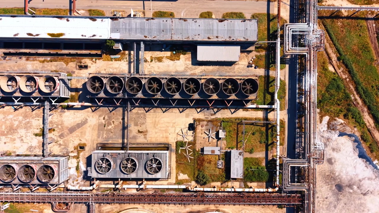 Ripresa aerea dall'alto di ventole di raffreddamento industriali e tubi. La vista dall'alto mostra file di unità di ventilazione rotonde, tubazioni metalliche, terreno in cemento