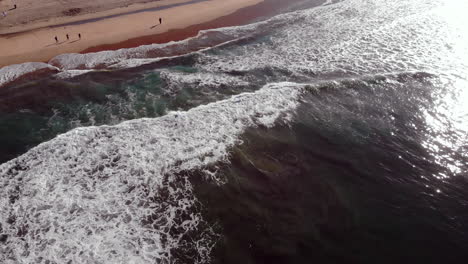 Aerial-4k-drone-flyover-from-surf-to-sand-over-waves-and-surfers-in-competition-at-Huntington-Beach-Pier-in-early-morning,-Pacific-Ocean,-Southern-California-to-people-on-the-beach