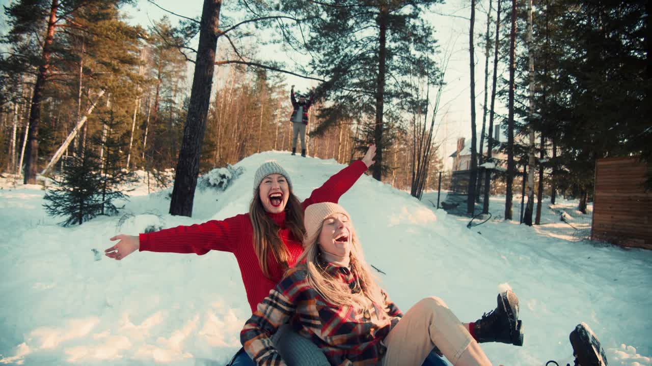 cámara lenta cinematográfica, dos hermosas mujeres felices emocionadas en trineo hacia la cámara en la pendiente del bosque de nieve soleada con los brazos levantados