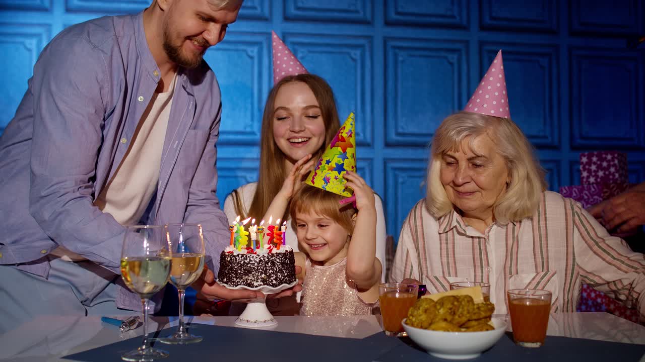 niña soplando velas en el pastel haciendo deseos, divirtiéndose, celebrando la fiesta de cumpleaños con la familia