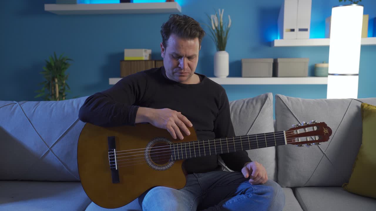 외로움으로 고통받는 남자는 집에서 혼자 기타를 연주하고 슬퍼합니다.