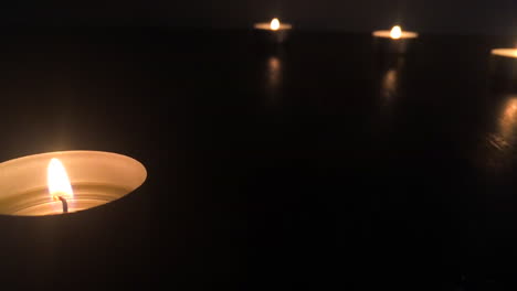 close angled view of four candles with static flames on a wooden table in the dark, in slow motion