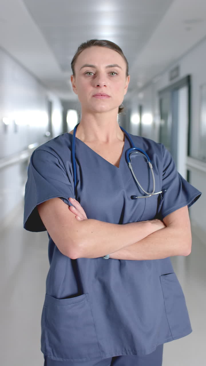 Vertical video of portrait of caucasian female doctor smiling in corridor, slow motion