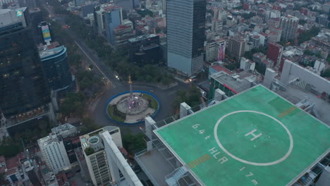 Drone-camera-flying-over-tall-office-building-with-green-heliport-on-top.-Aerial-view-of-city-near-Angel-of-Independence-monument.-Mexico-city,-Mexico.