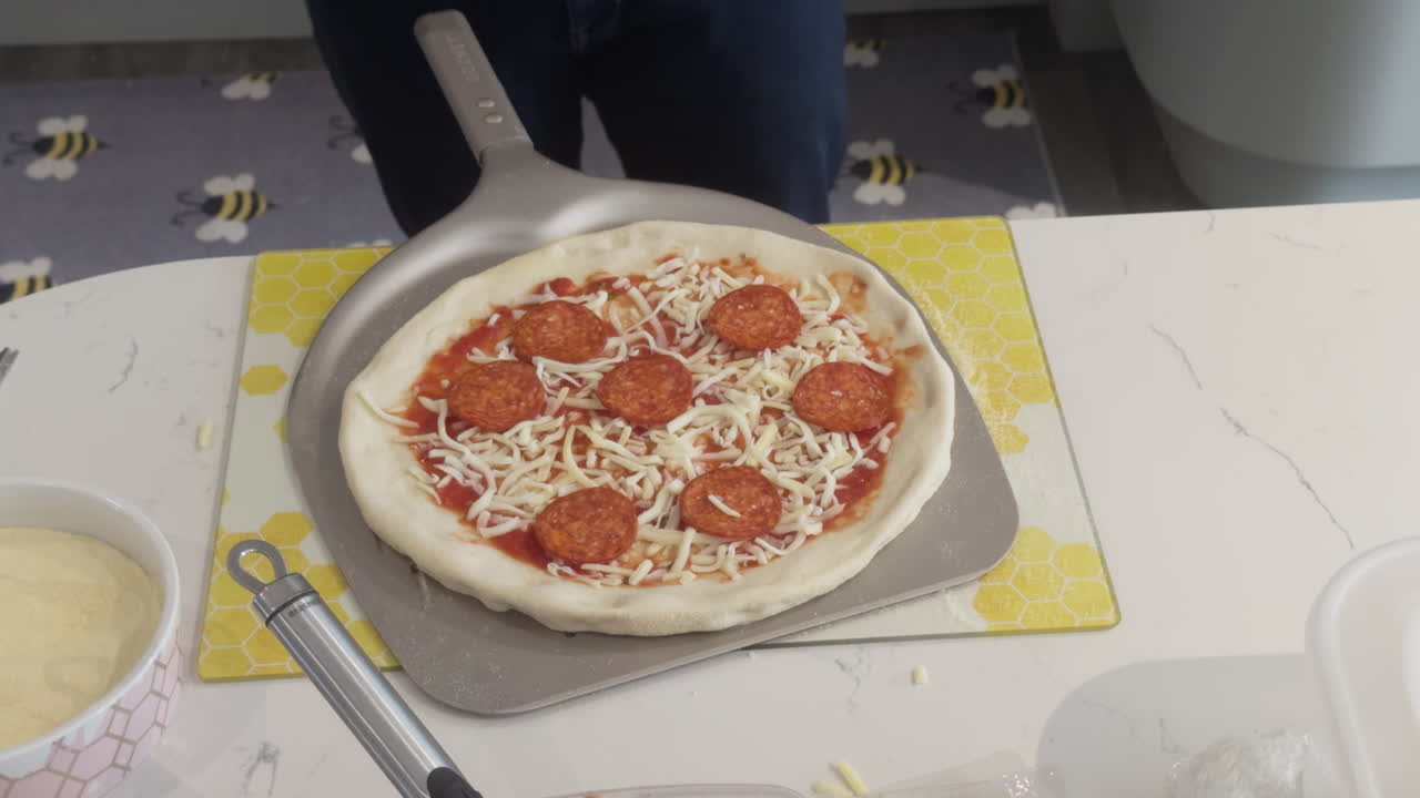 Close-up of assembling a delicious pepperoni pizza with cheese and sauce on a kitchen table.