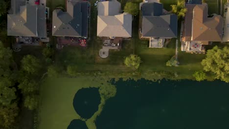 establishing aerial drone view of suburban homes by a serene lake in illinois, showcasing a peaceful neighborhood with well-maintained lawns and picturesque waterfront scenery
