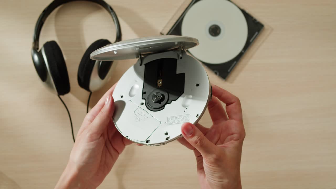 manos sosteniendo un reproductor de cd portátil con auriculares y un cd