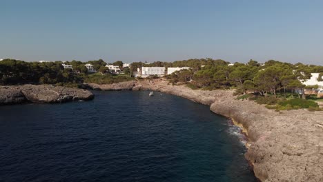 AERIAL:-flying-in-small-bay-close-to-the-sea-cliffs-and-trees-with-boat