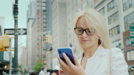 Eine-Junge-Frau-Benutzt-Ein-Smartphone-Vor-Dem-Hintergrund-Von-Bürogebäuden-In-Der-Innenstadt-Von-Manhattan-New-Ytan