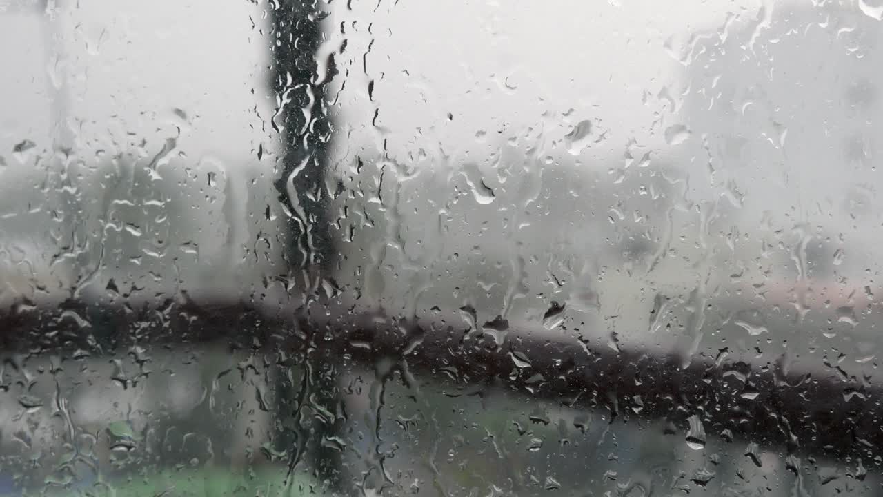 fuerte agua de lluvia se derrama contra el vidrio de la ventana y fluye hacia abajo, de cerca. gotas de lluvia en fondo de vidrio en la temporada de lluvias. 4k