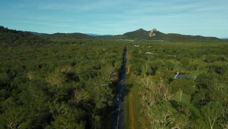 Silbernes-Auto,-Das-Auf-Der-Straße-Entlang-Eines-üppigen-Grünen-Eukalyptuswaldes-Und-Der-Berge-Fährt