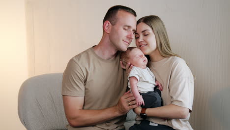 happy family of three together. caucasian parents hold their sleeping newborn and lean to him.