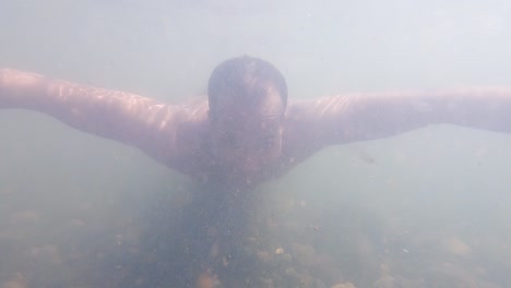 Mann-Schwimmt-Im-Schmutzigen-Wasser-Des-Flusses,-Unterwasseransicht-Mit-Sonnenlichtstrahlen-Am-Morgen