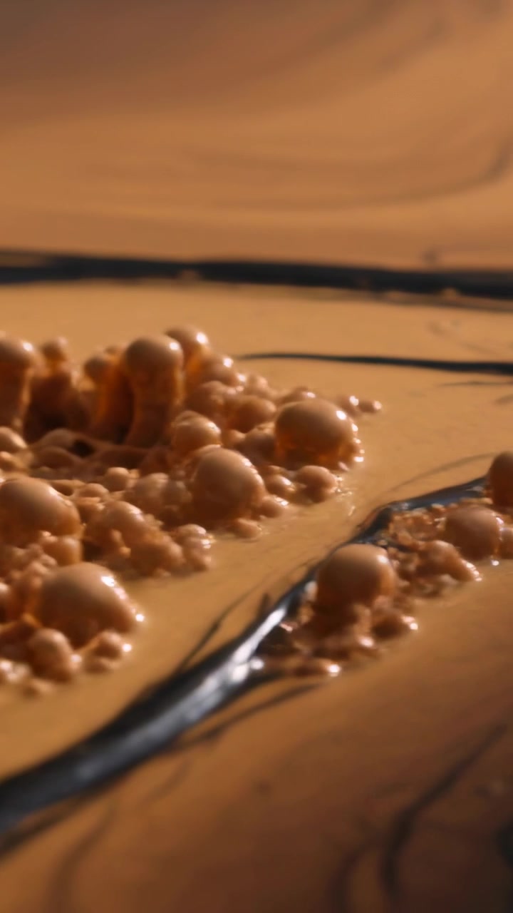 Video verticale: Iniziando con piccole bolle centrali, un cumulo di bolle beige che sale su un vassoio, con striature scure.