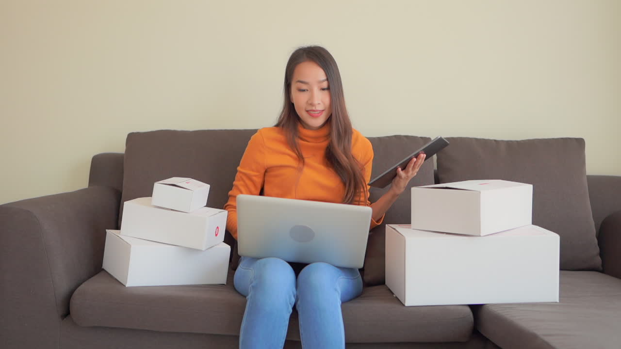 las cajas rodean a una mujer joven con una tableta en una mano y una computadora portátil en las piernas ingresa datos y dramáticamente con un puño cuando termina de escribir