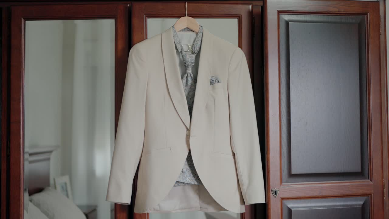Beige suit jacket hanging on a hanger inside a room, displayed against a wooden wardrobe