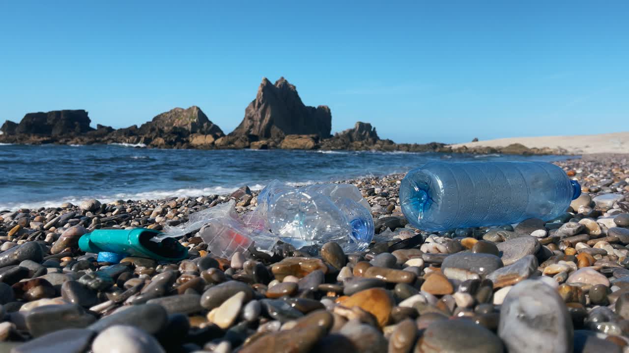 botellas de plástico y basura esparcidas en una playa rocosa cerca del océano