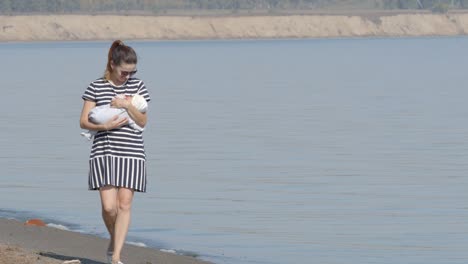 young mother walks with her infant on a coast in sunny day